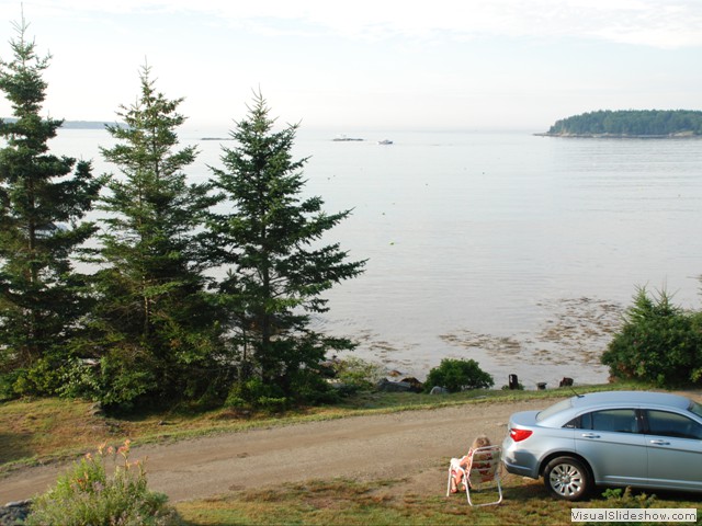 July 28: Nancy enjoys coffee and morning sun in front of the cottage.  Rental car at right.
